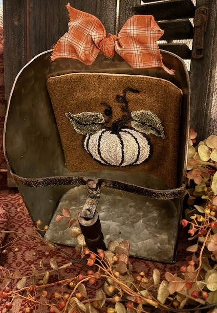 Punch needle pumpkin on harvest gold wool held in an antique seed scoop