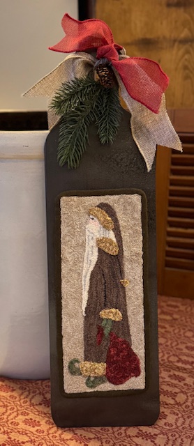 Punch needle Saint Nick mounted to a wooden hornbook with greens and ribbon