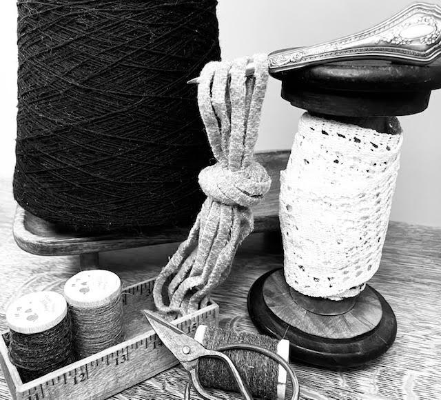 Still life of fiber crafting tools: yarn cone, wool braid, antique spools and scissors